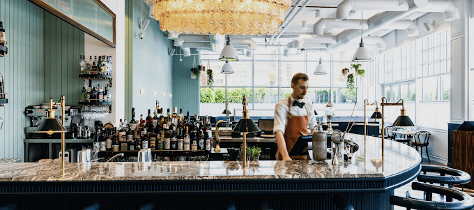 Bartender at the marble bar inside Maine Street Eatery, Studio City, Dubai, with elegant decor and large windows.
