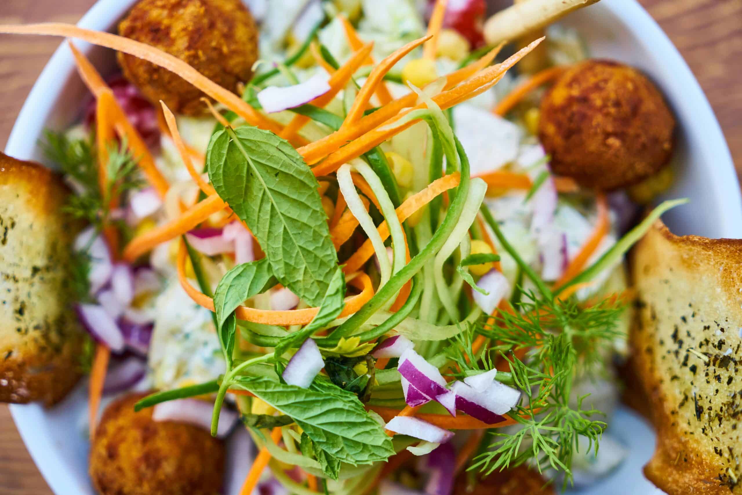 Vibrant salad featuring fresh vegetables, falafel, and herbs in a white bowl, perfect for a healthy meal.