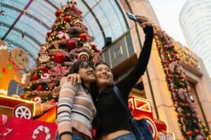 Two women taking a selfie in front of festive Christmas decorations at Ibn Battuta Mall.