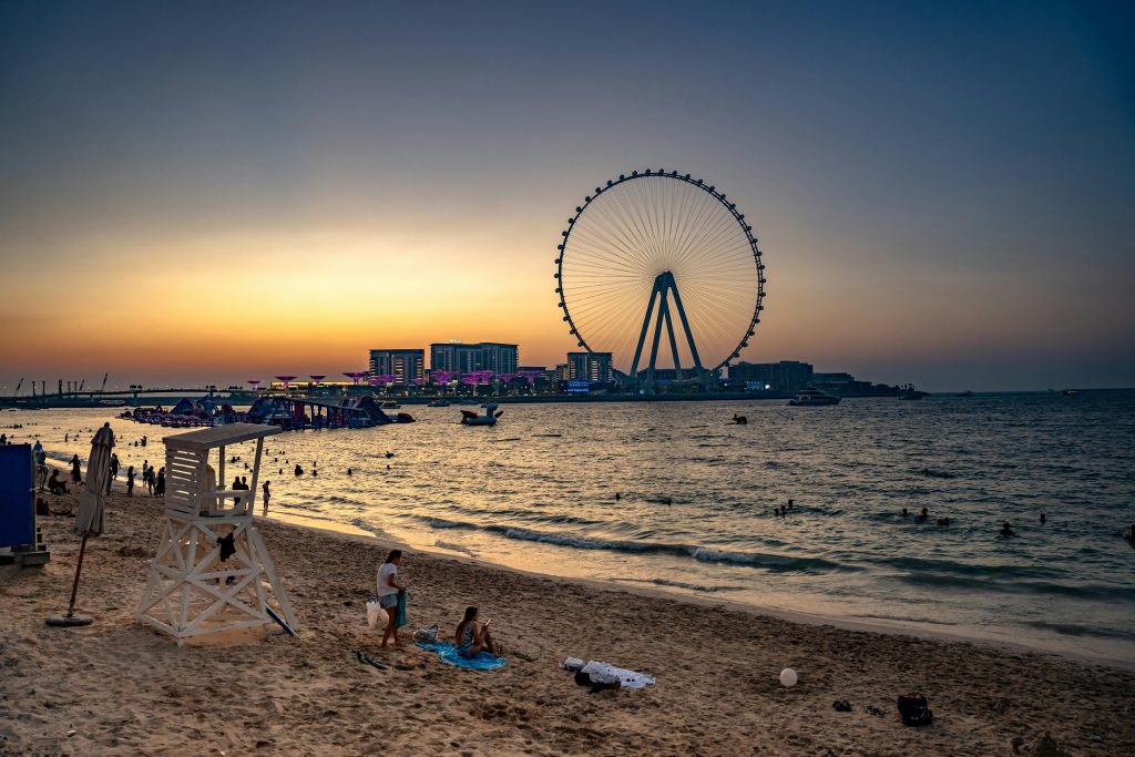Serene sunset with Dubai Eye and beachgoers enjoying the evening by the water.