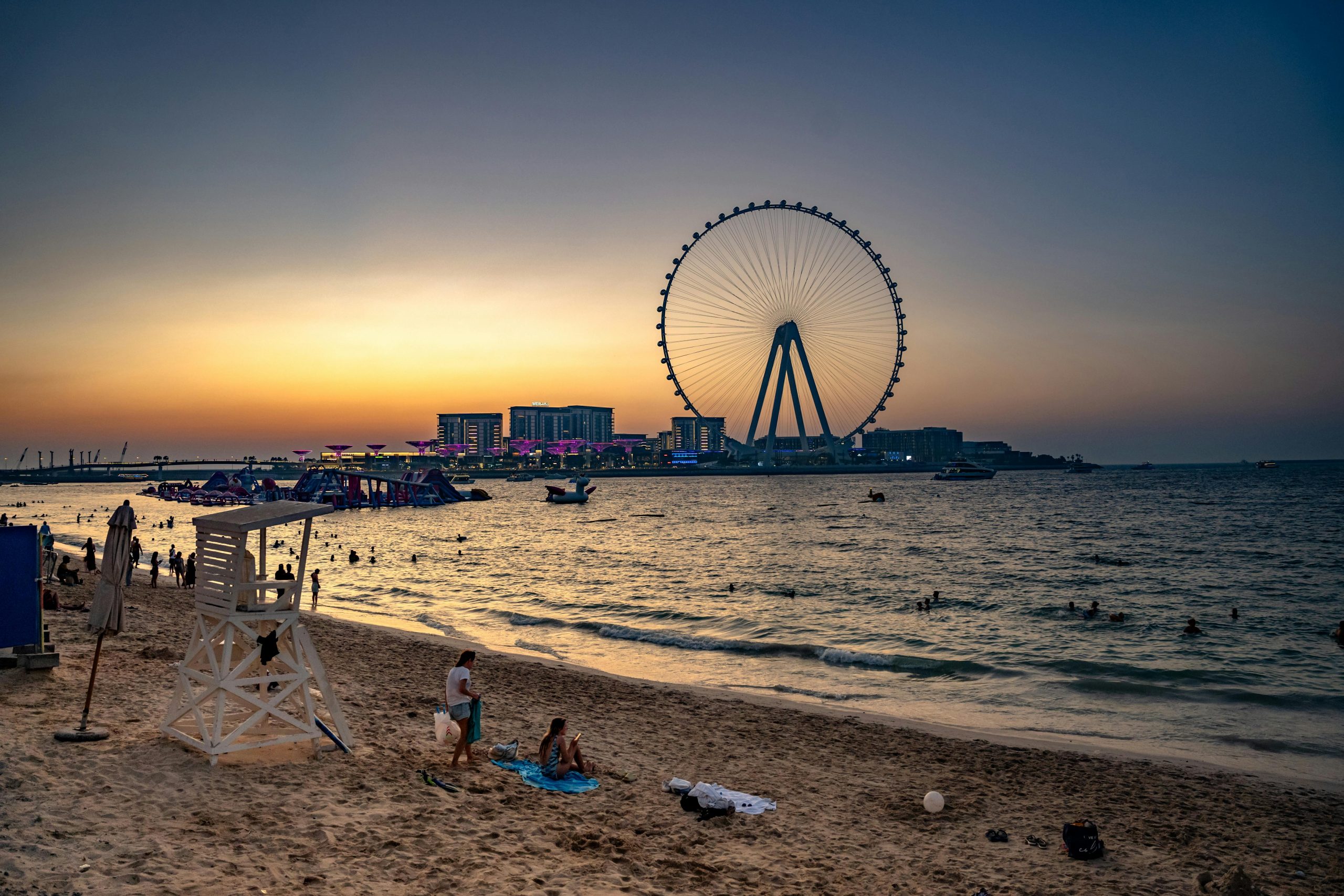 Serene sunset with Dubai Eye and beachgoers enjoying the evening by the water.